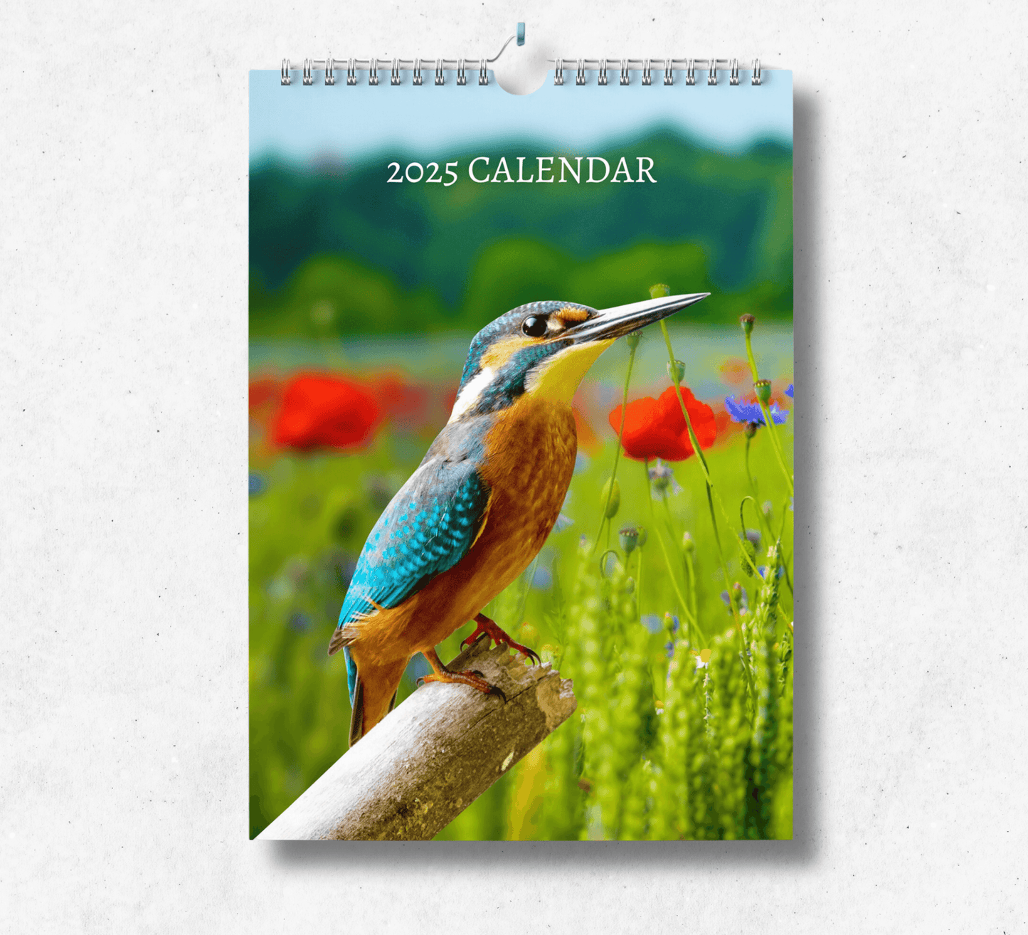 2025 Garden Birds calendar featuring a kingfisher perched on the end of a broken tree branch, with a blooming grass background full of red flowers.