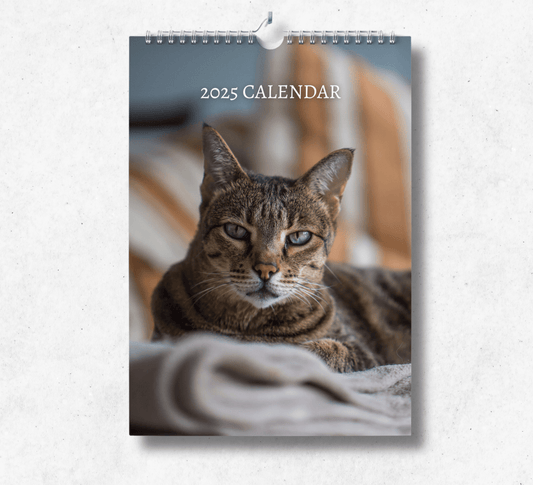 2025 Savannah Cat  calendar featuring a beautiful brown savannah cat laying down on a grey blanket, looking straight into the camera.